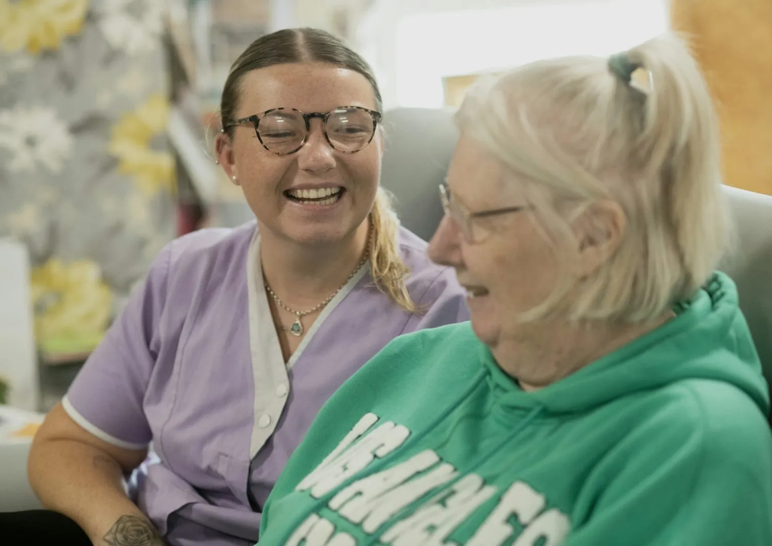 A caregiver sitting with an older woman, both smiling.
