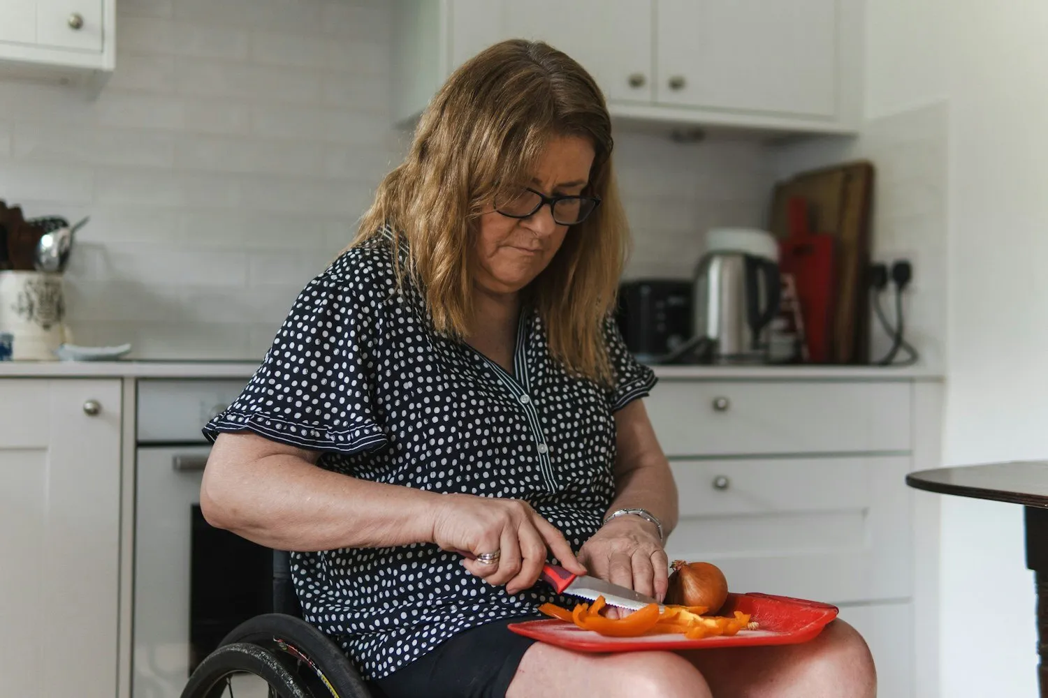 A woman in a wheelchair chopping vegetables at her own kitchen counter.