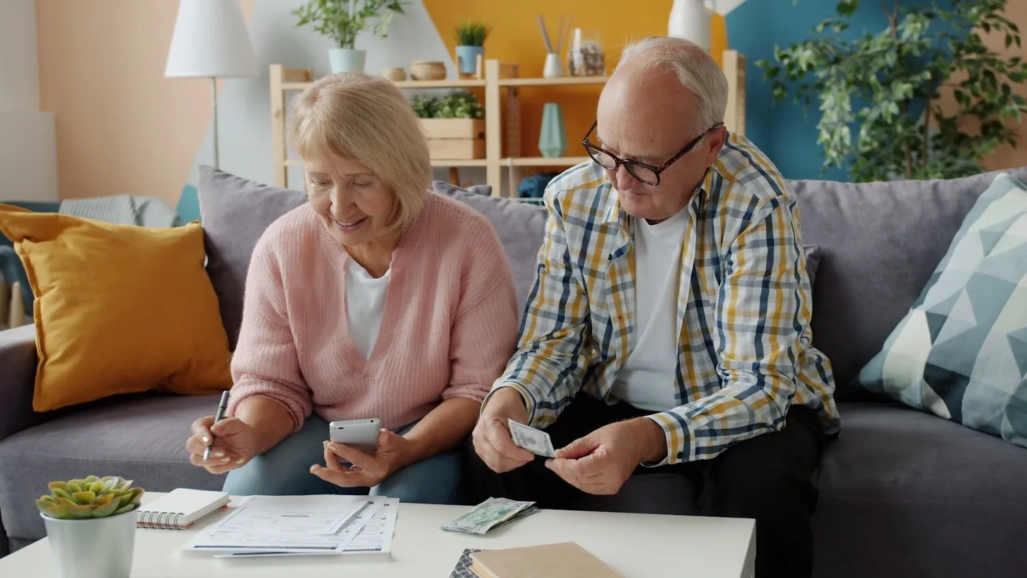 An older couple going through paperwork on their sofa with a phone and notepad.