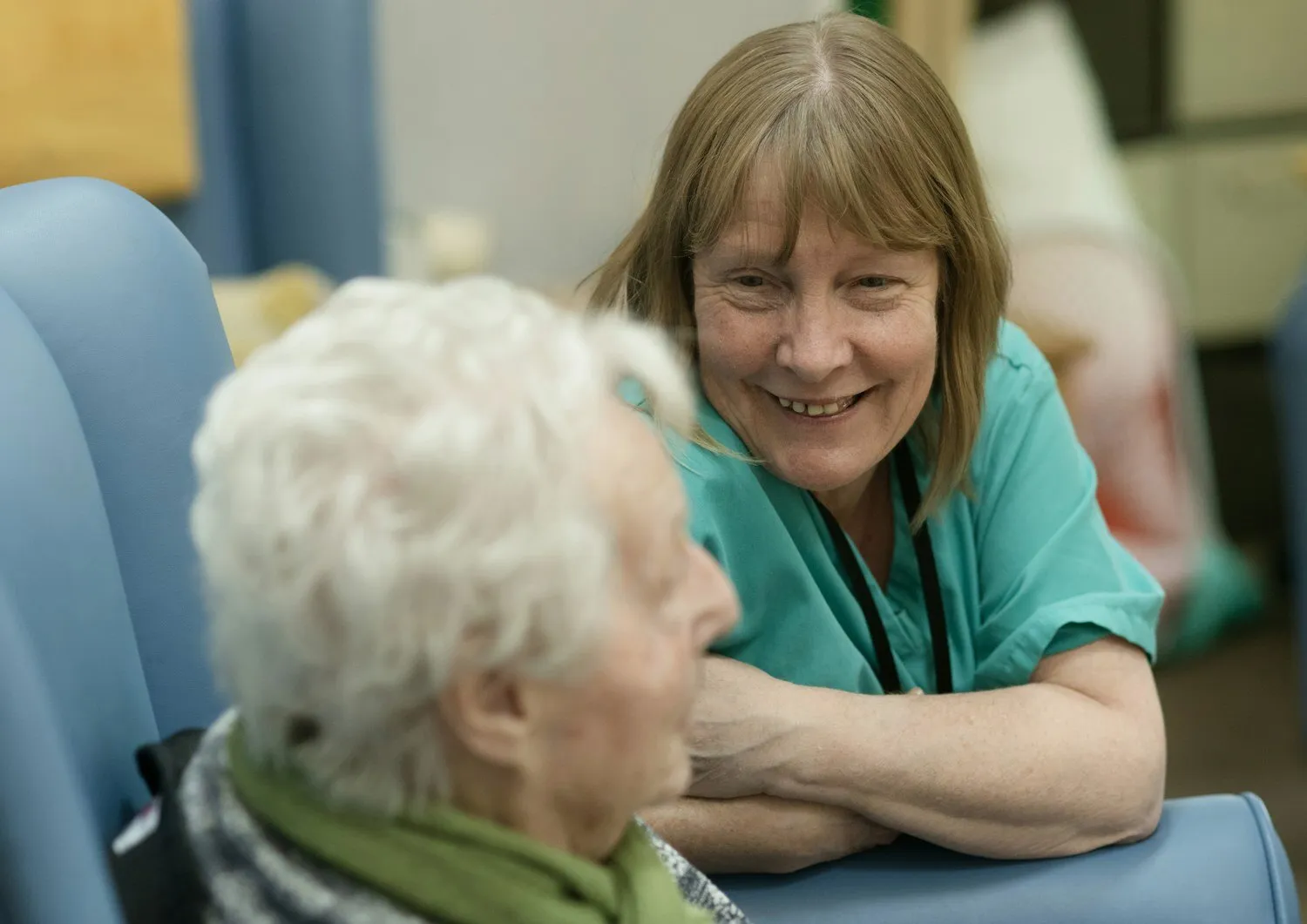 A care worker leaning in to talk with an older woman, both smiling.