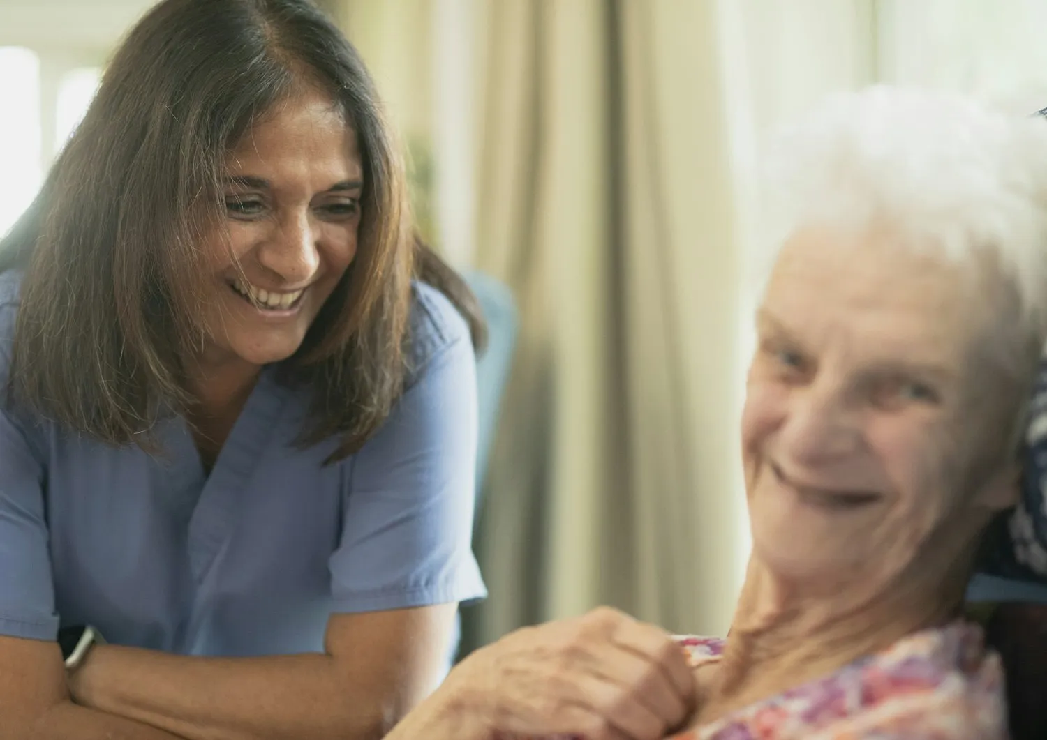 A nurse and an older woman laughing together during a home visit.