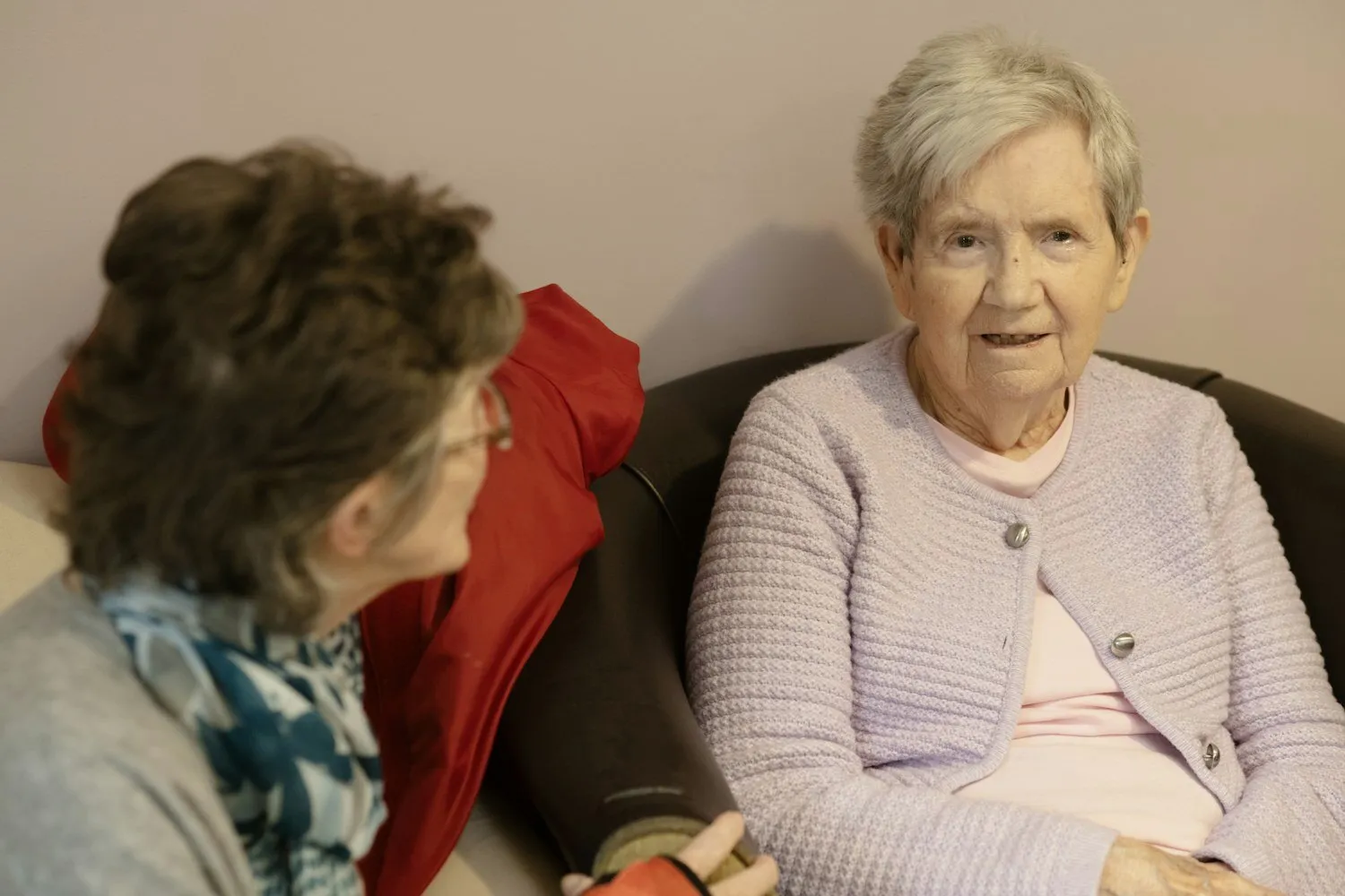 Two women sitting close together on a sofa, talking.